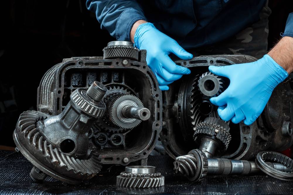 Hands of a male repairman in blue gloves on a background of a gearbox, close-up. Repair box predach, repair of used cars. Metal background.